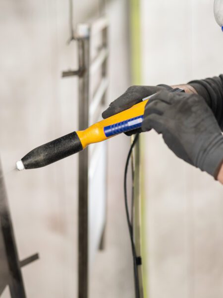 The detail of a man working in a factory finishes a job using the technique of electrostatic powder coating with a spray gun.