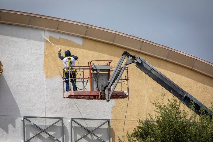 Commercial painting worker painting a yellow wall white using a paint sprayer while standiong on a manlift