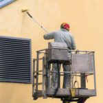 Commercial Exterior Painter lifting platform painting the building wall with a roller exterior outdoors.