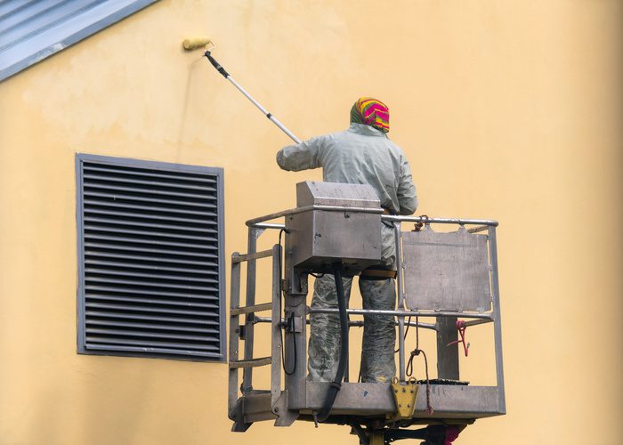 Commercial Exterior Painter lifting platform painting the building wall with a roller exterior outdoors.