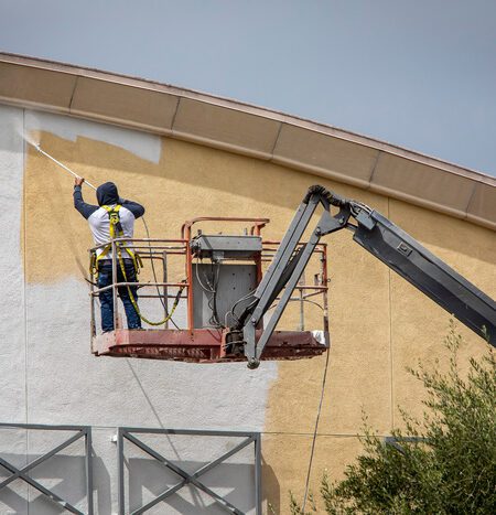 Man painting a yellow wall white using a paint sprayer while standing on a manlift