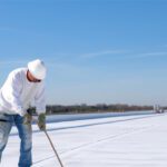 Worker applies an insulation silicon coating on the concrete surface of a rooftop.