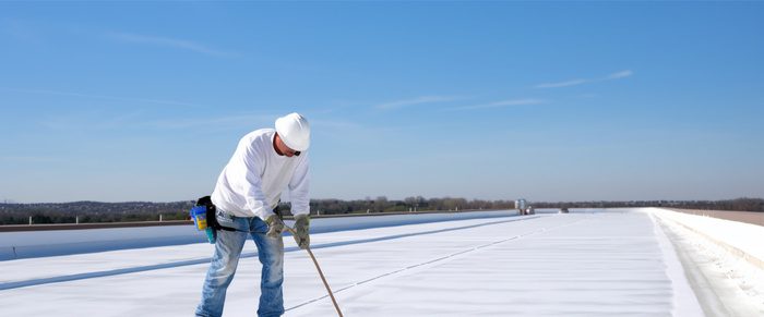 Worker applies an insulation silicon coating on the concrete surface of a rooftop.